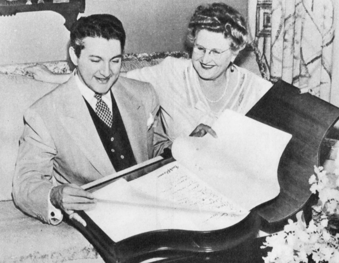 Liberace holds a book whilst sitting next to his mother