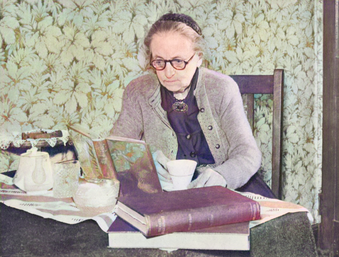 A woman sits at a table, reading and drinking a cup of tea